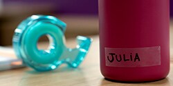 Botella con etiqueta sobre un escritorio junto a Cinta Mágica Cool Colors.
